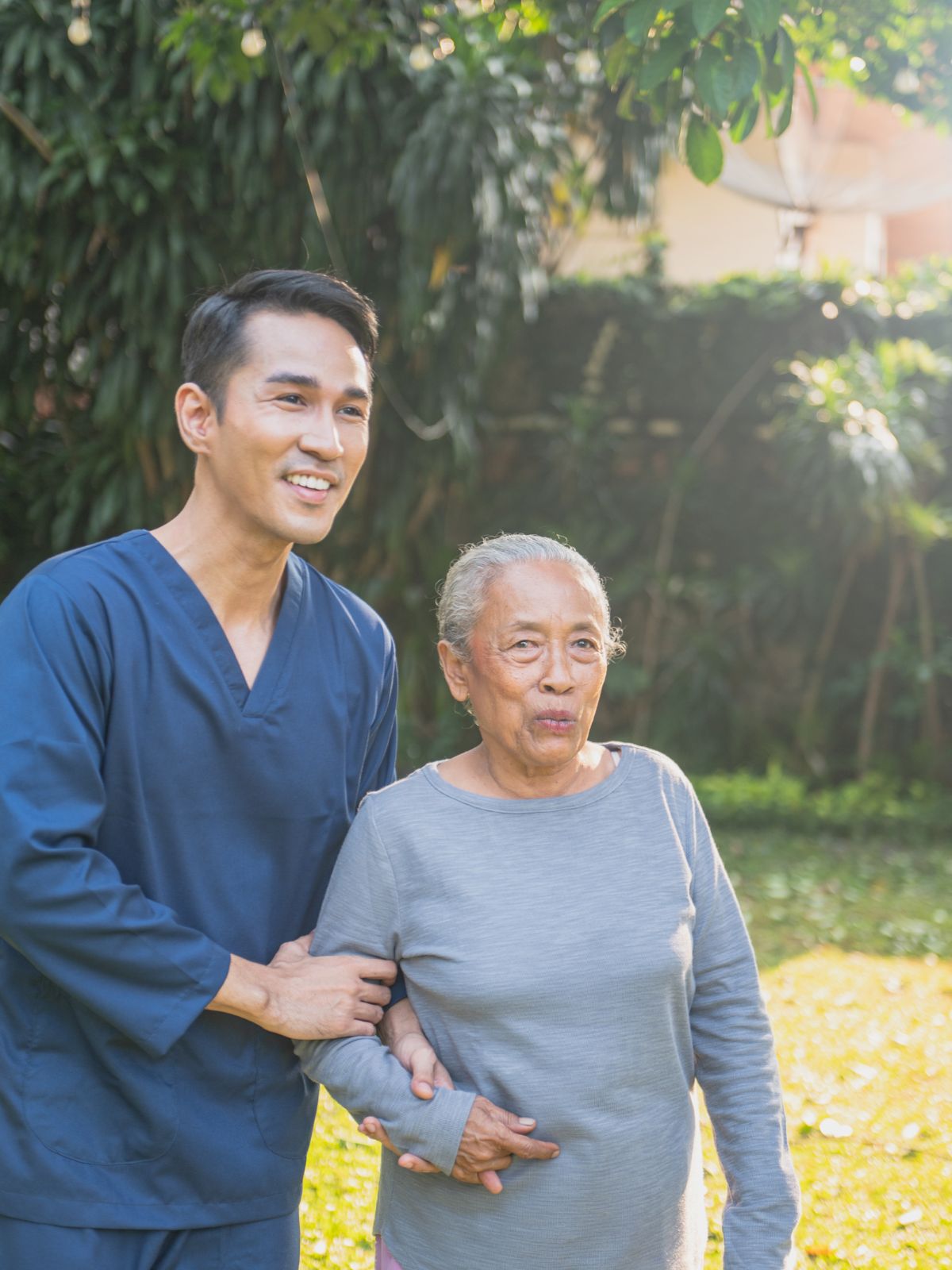 Caregiver supporting an elderly woman during a walk outdoors